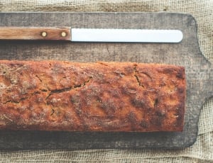 baked bread beside bread knife on black wooden tray thumbnail