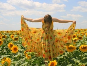 women  wearing   sunflower printed  dress standing in sunflower under cloudy weather during daytime thumbnail