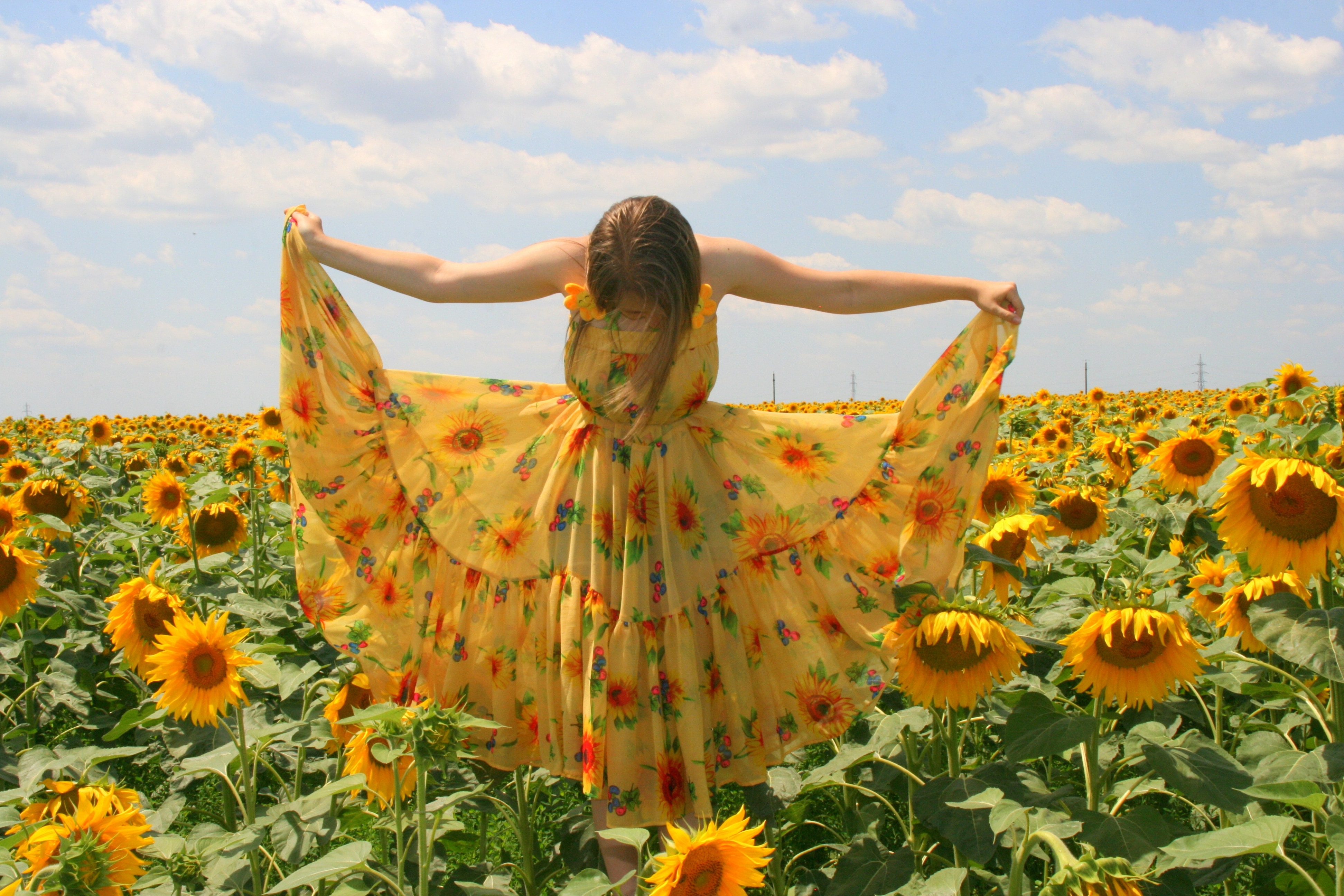 women  wearing   sunflower printed  dress standing in sunflower under cloudy weather during daytime