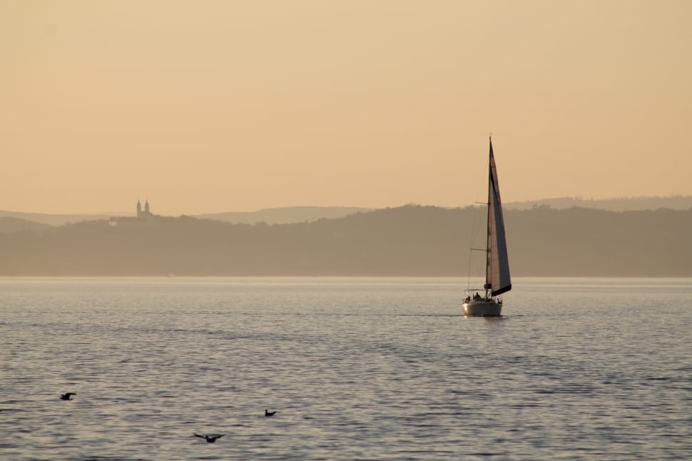 white sail boat on sea near black mountain during daytime preview
