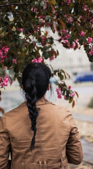 close up photo of a woman in brown jacket standing near the pink flowers thumbnail