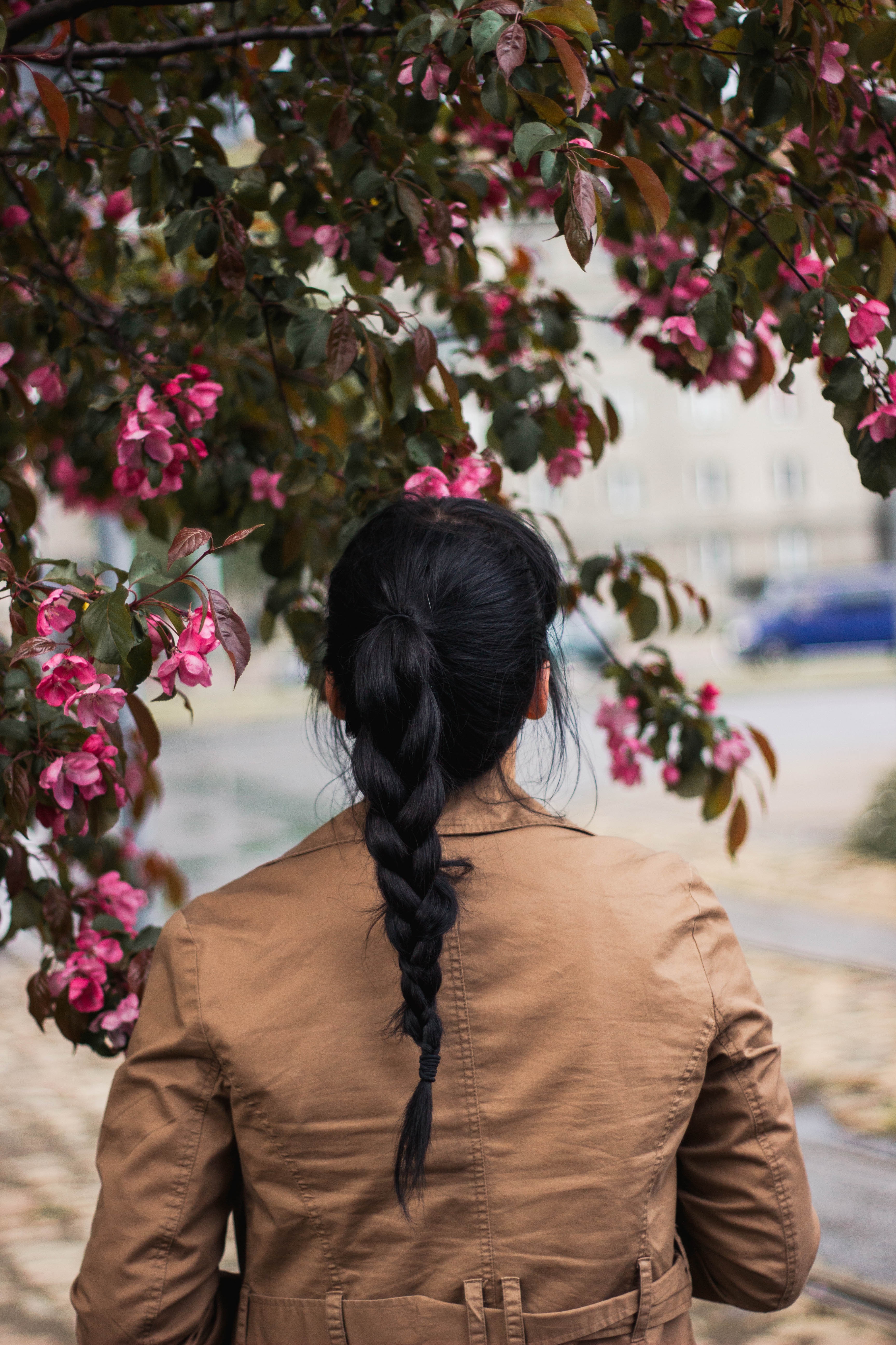 close up photo of a woman in brown jacket standing near the pink flowers