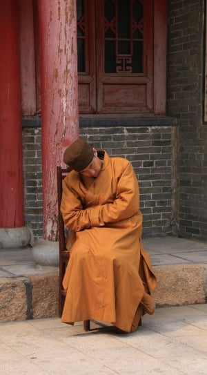 monk sitting on chair near post during daytime thumbnail