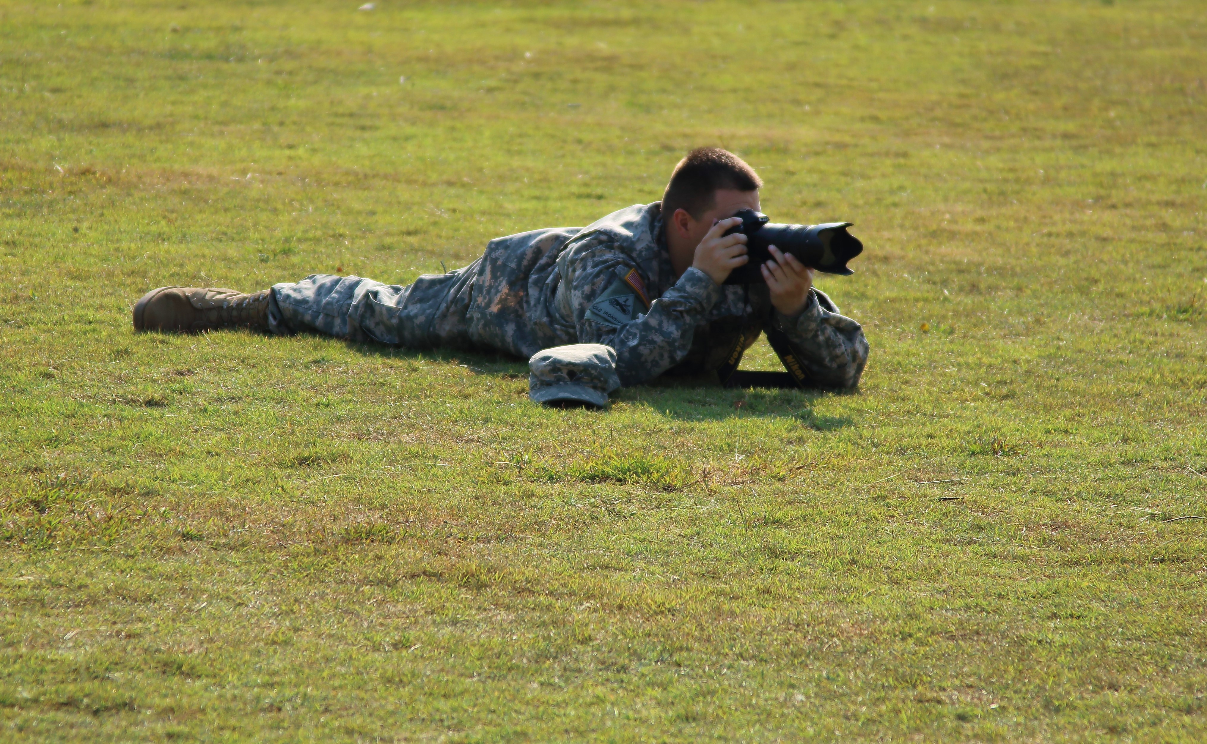 man in camouflage soldier uniform holding bridge camera lying on grass at daytime