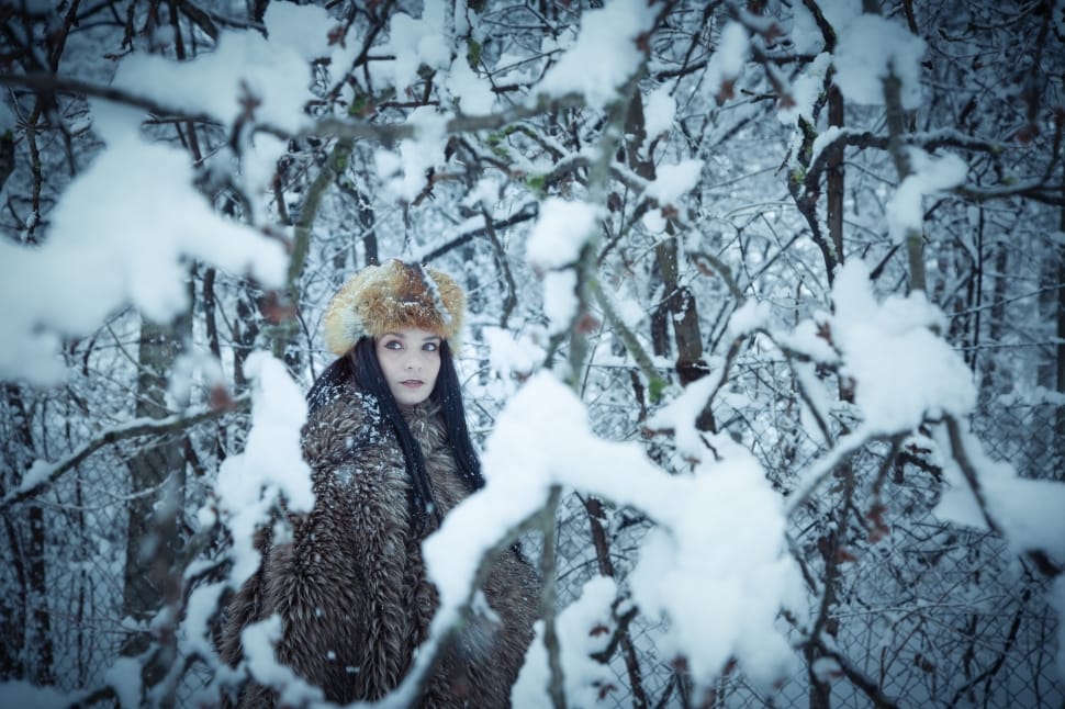 woman in brown faux fur coat and in snow covered woods preview