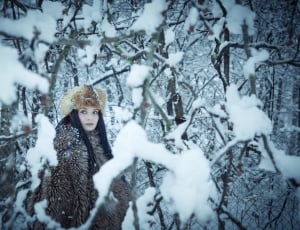 woman in brown faux fur coat and in snow covered woods thumbnail