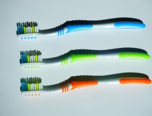 three blue, green, and orange tooth brush on white surface thumbnail