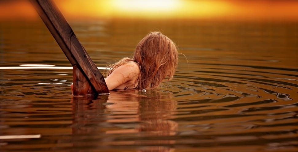 woman half dip on body of water near brown wooden handle preview