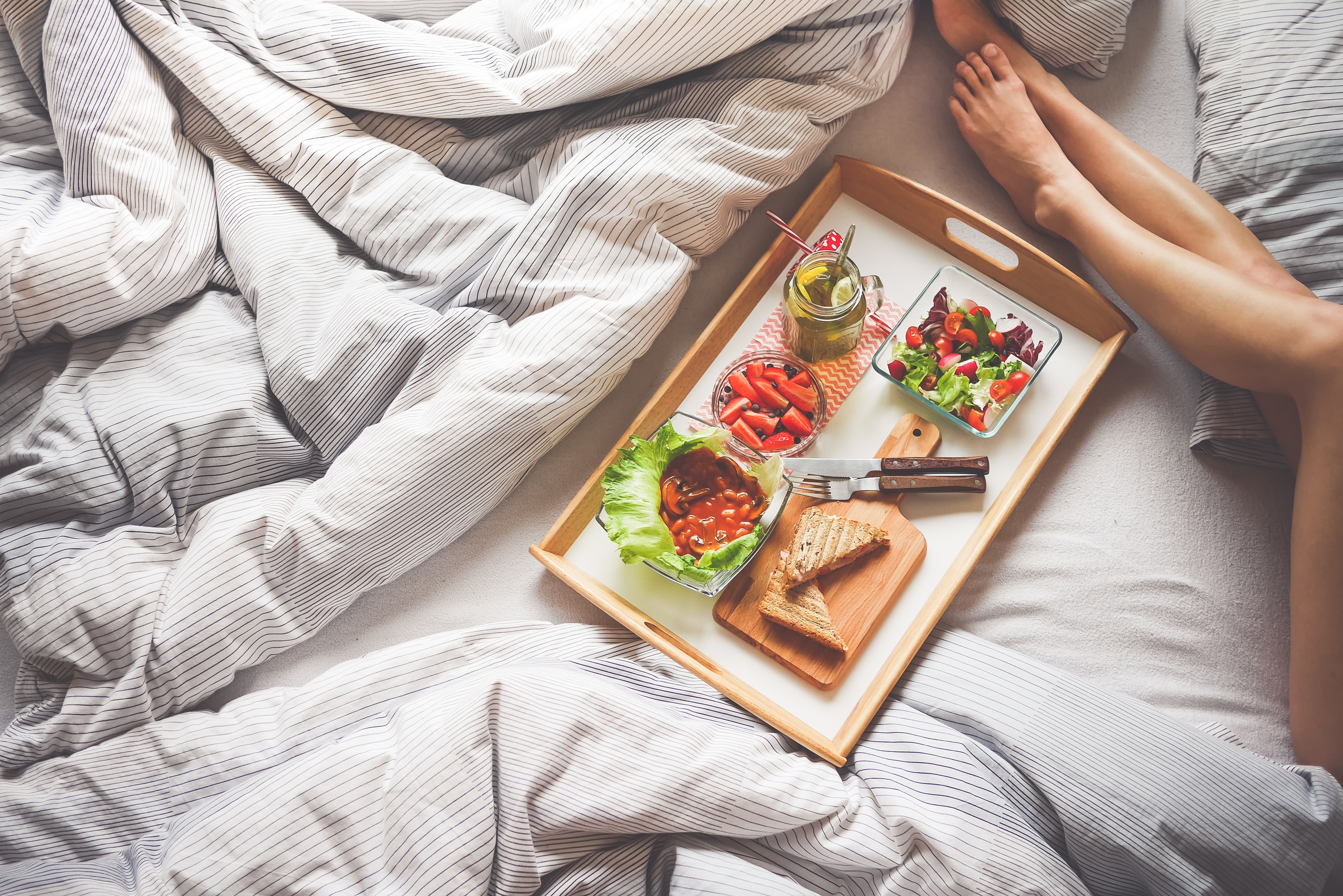 person laying in bed near brown serving tray filled with fruits and sandwich