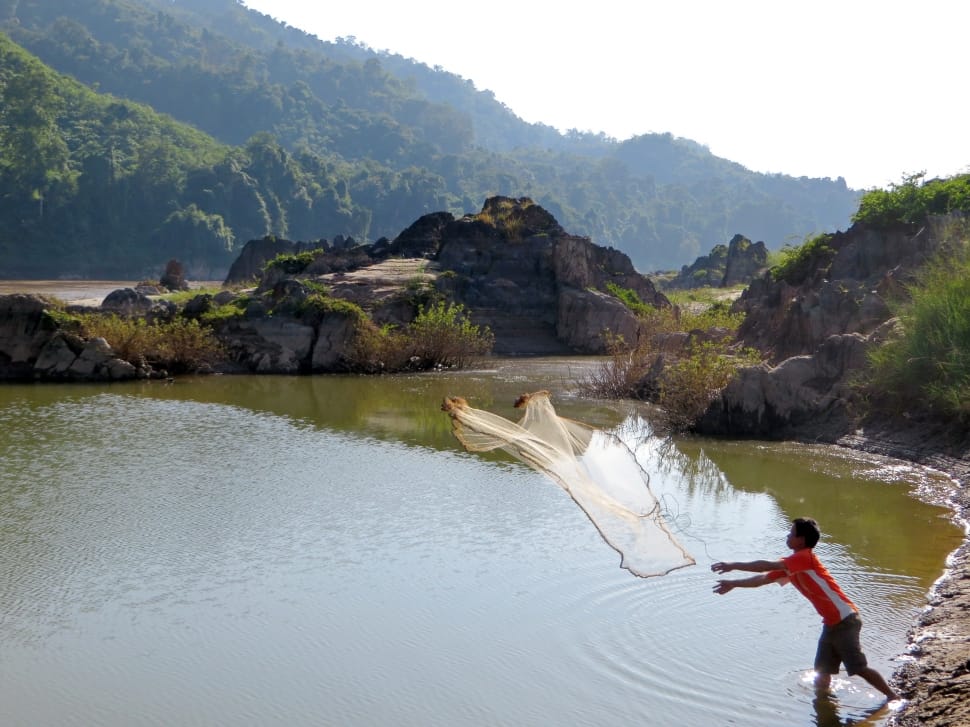 man in red t shirt throwing fishing net on river during daytime preview