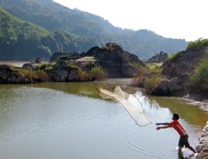 man in red t shirt throwing fishing net on river during daytime thumbnail