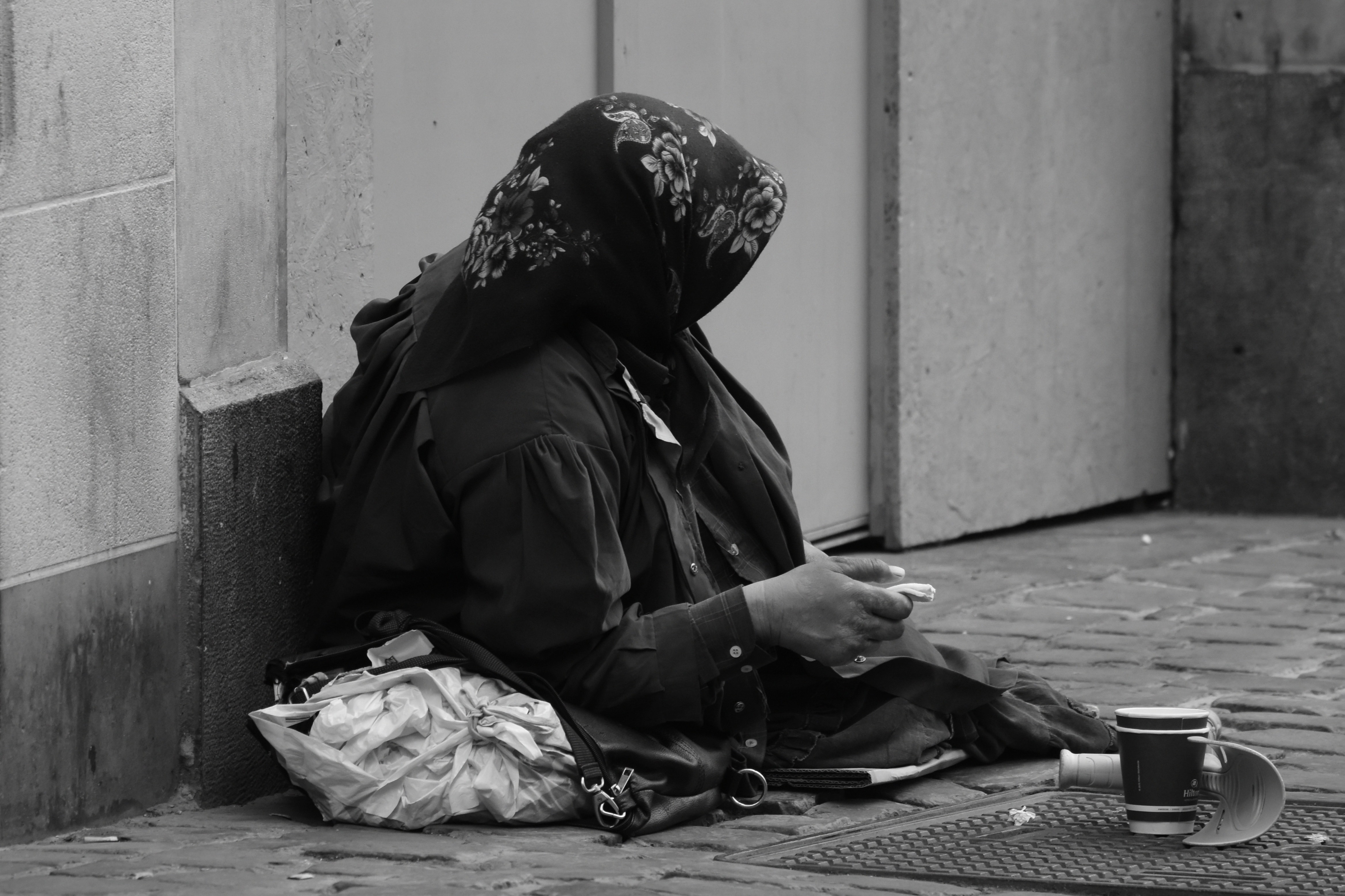 grayscale photo of person in black coat sitting on pavement