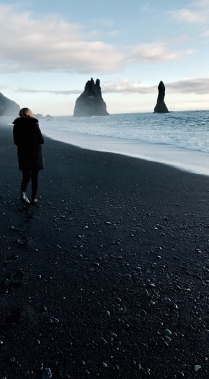 woman in black fur trim coat walking on seashore during daytime photo thumbnail