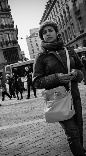 gray scale photo of woman walking beside buildings thumbnail