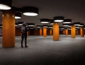man wearing black hooded furline jacket in wide room with lighted and pillars thumbnail