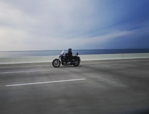 selective focus photography of man riding motorcycle near body of water under blue skies thumbnail