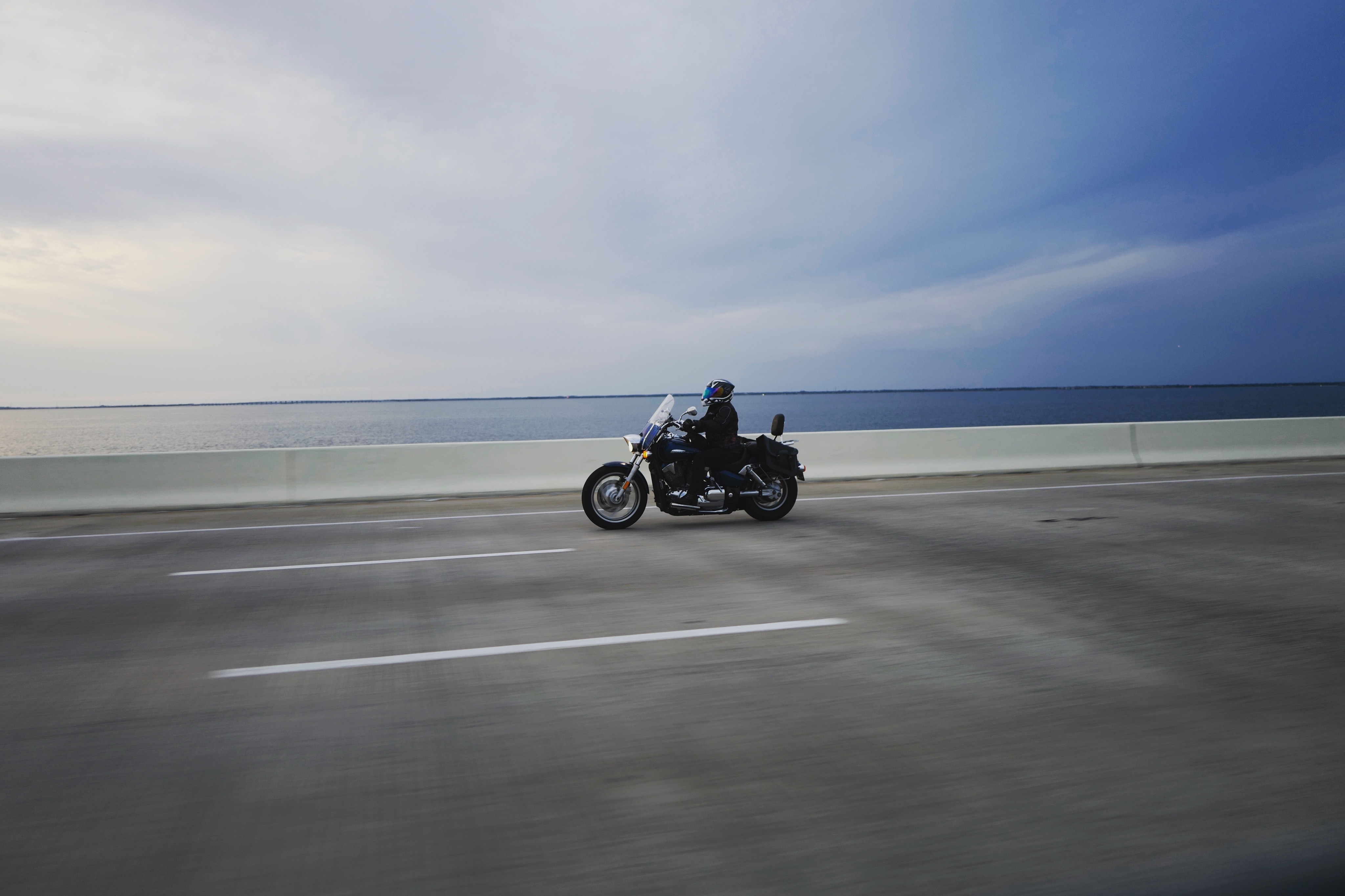 selective focus photography of man riding motorcycle near body of water under blue skies