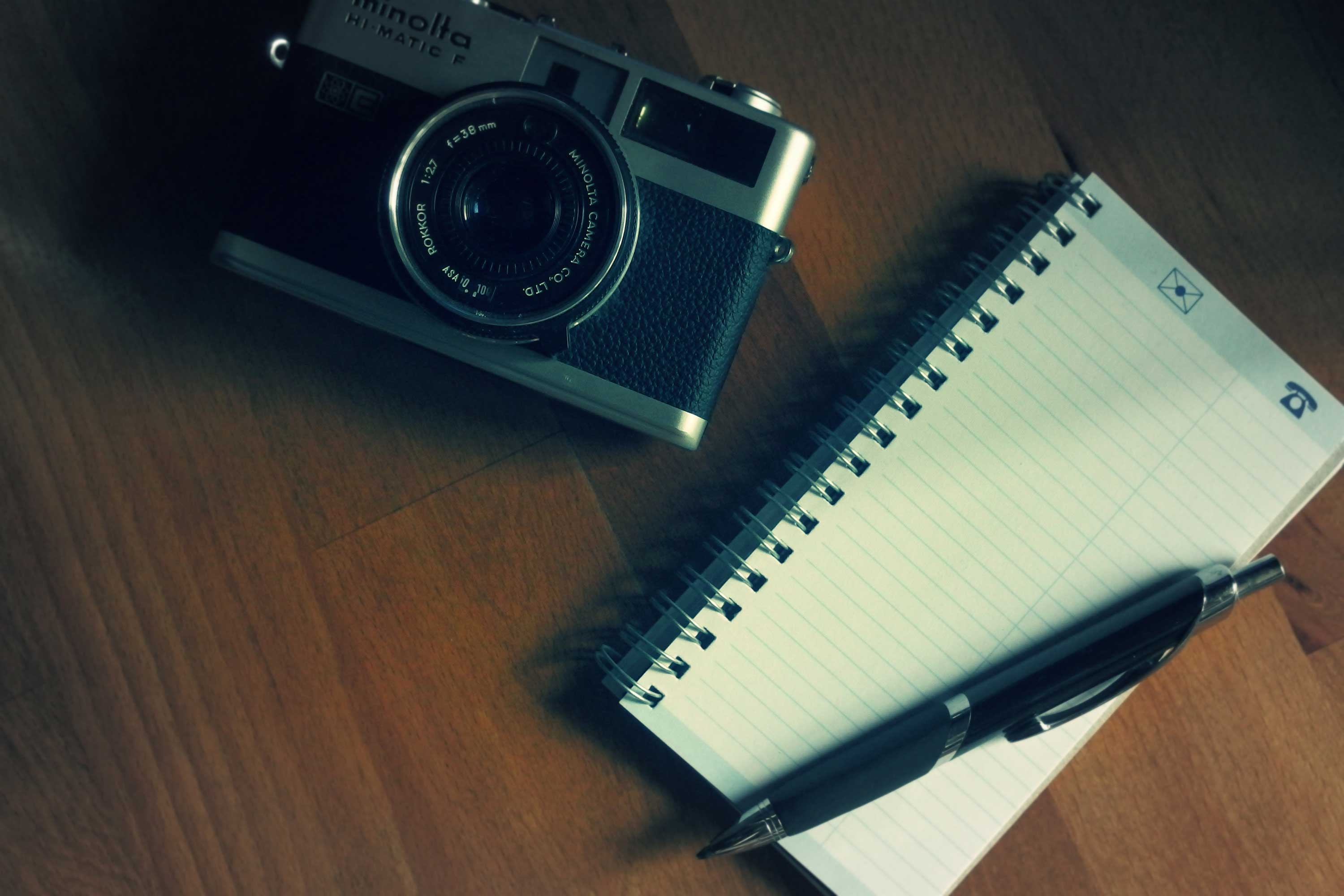 white spiral notebook click pen and minolta camera