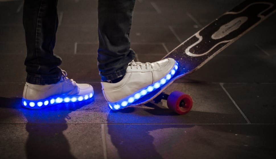 human wearing pair of white led sole sneakers stepping on to long board preview