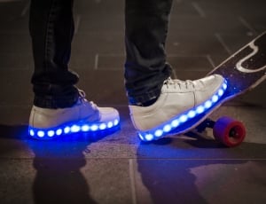 human wearing pair of white led sole sneakers stepping on to long board thumbnail