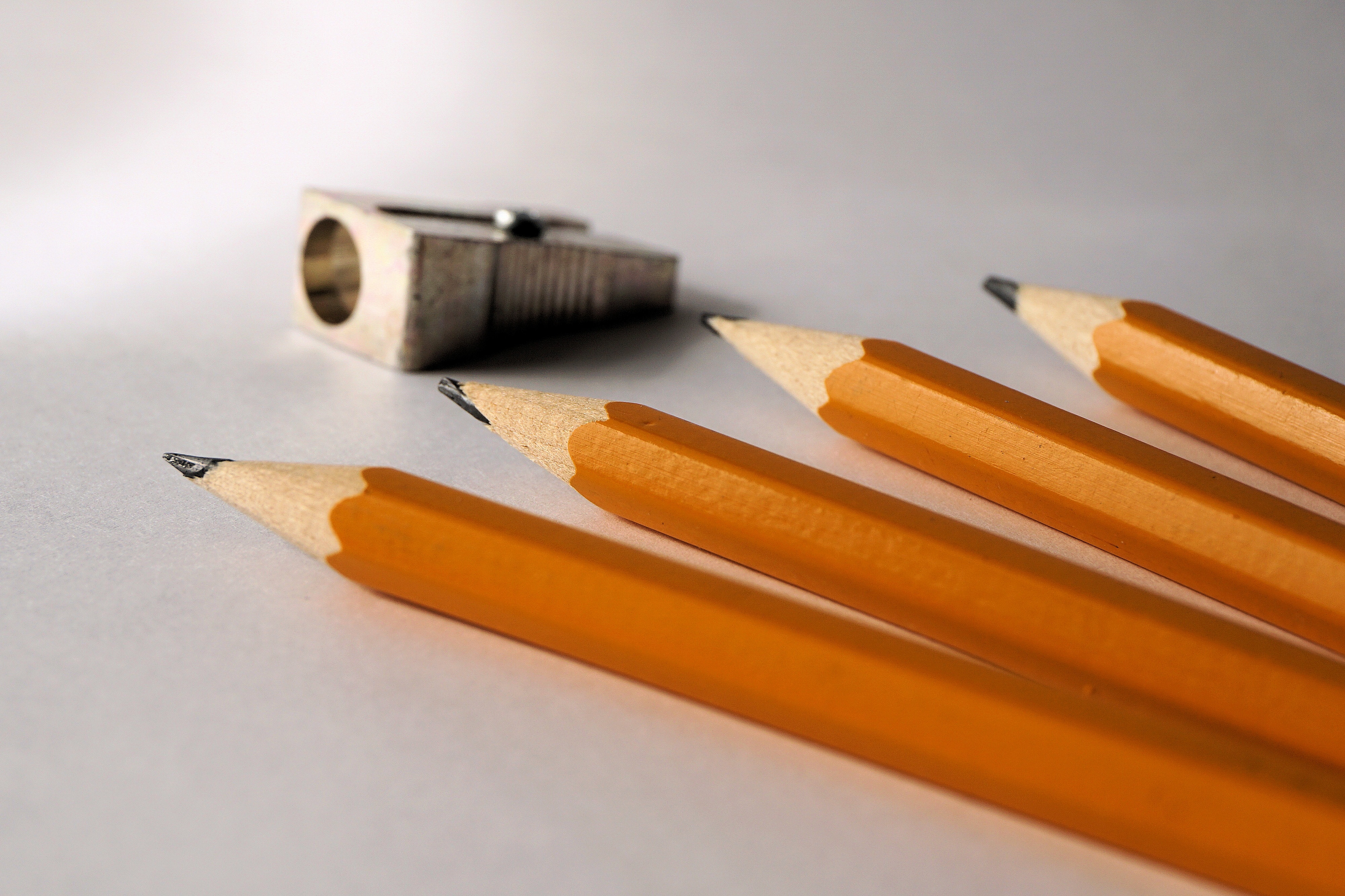 four yellow pencils beside gray metal sharpener