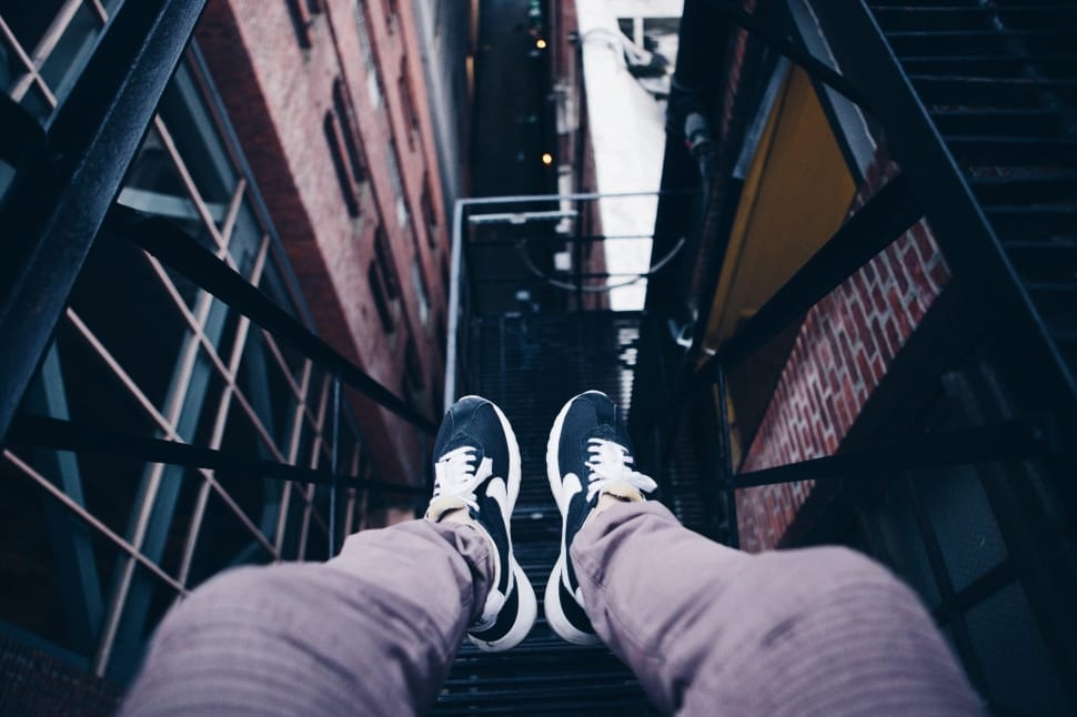 person wearing gray jeans and blue sneakers sitting in front of high rise buildings preview