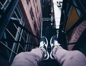 person wearing gray jeans and blue sneakers sitting in front of high rise buildings thumbnail
