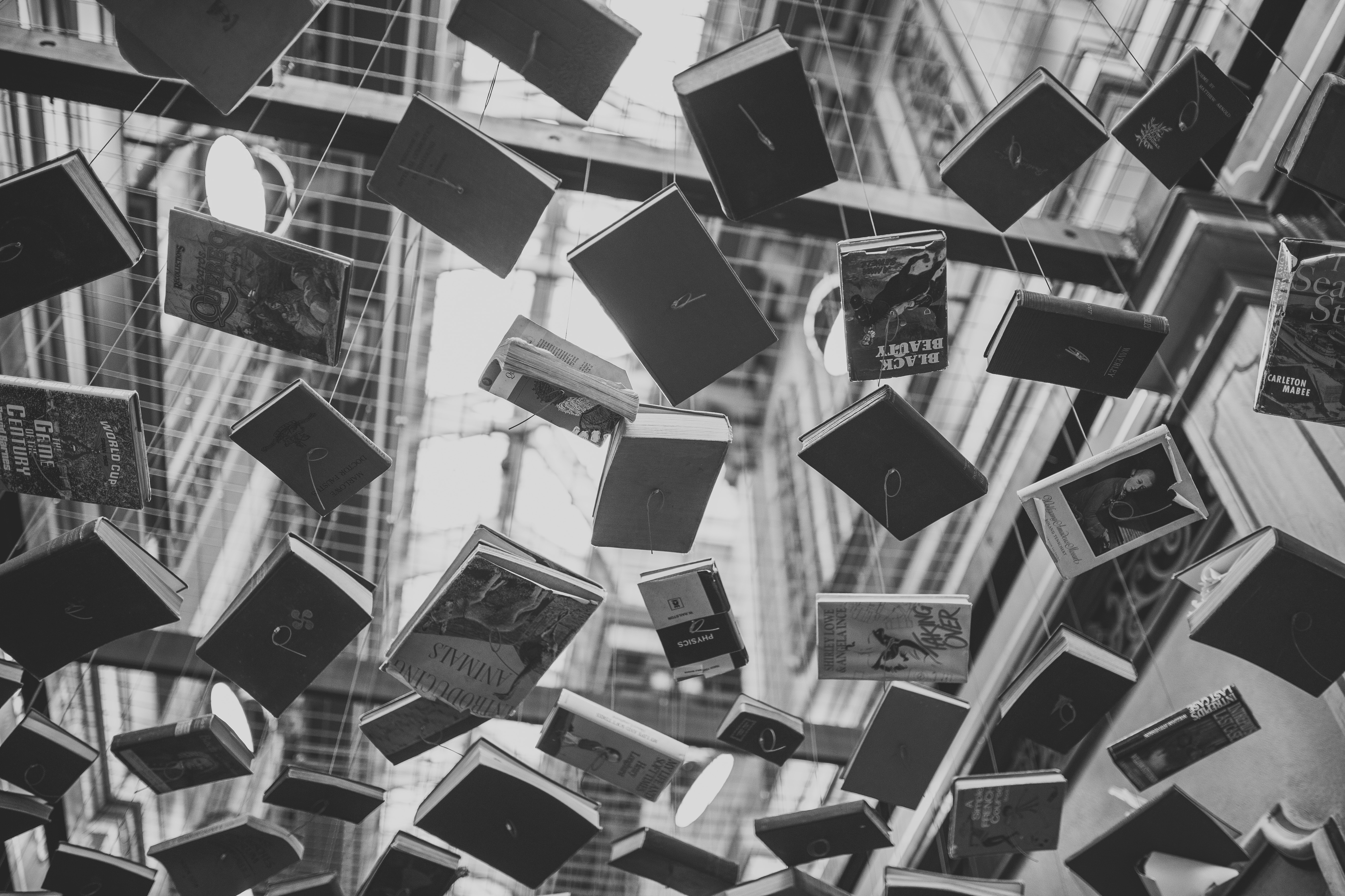 grayscale photo of assorted books hanging on the air