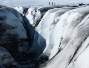 three person walking on ice covered mountain range near slope thumbnail
