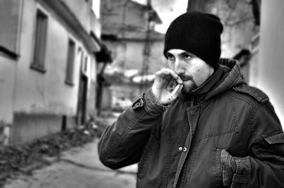 man smoking cigarette wearing knit cap near buildings preview