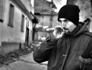 man smoking cigarette wearing knit cap near buildings thumbnail