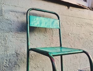 green metal chair in front of gray wall thumbnail