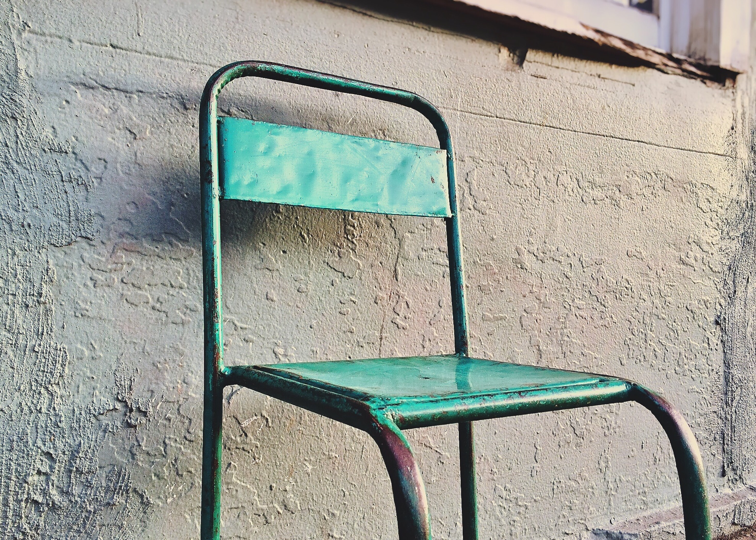 green metal chair in front of gray wall