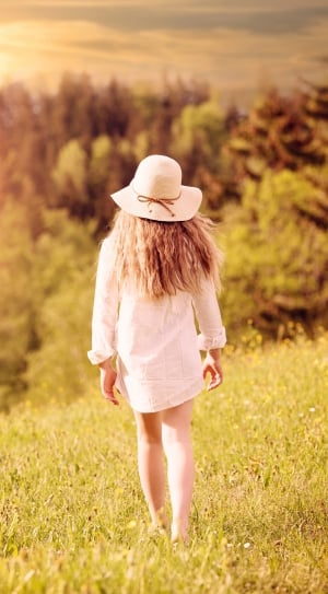 selective focus photography of woman in white long sleeve top and brown wicker hat walking towards the woods thumbnail