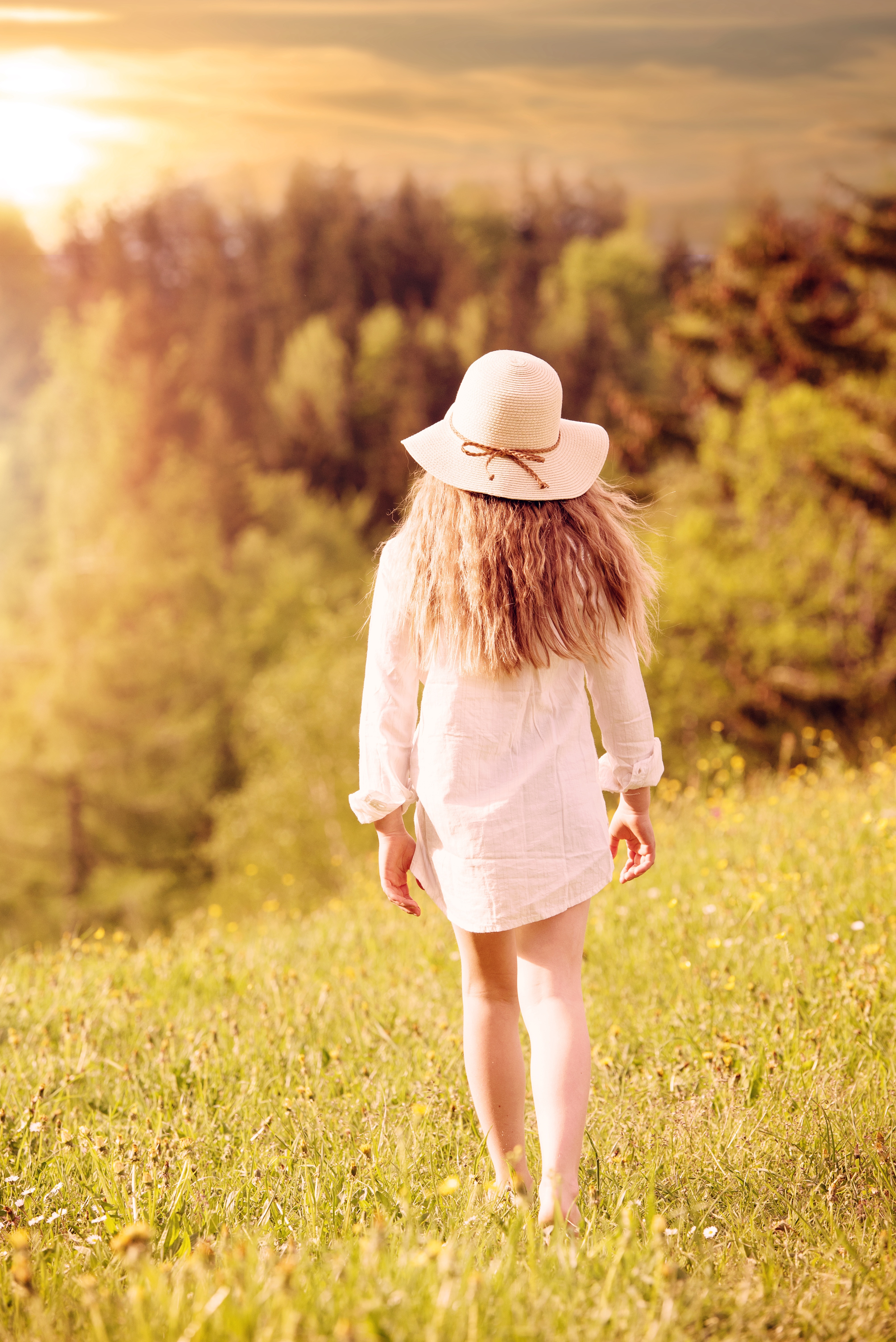 selective focus photography of woman in white long sleeve top and brown wicker hat walking towards the woods