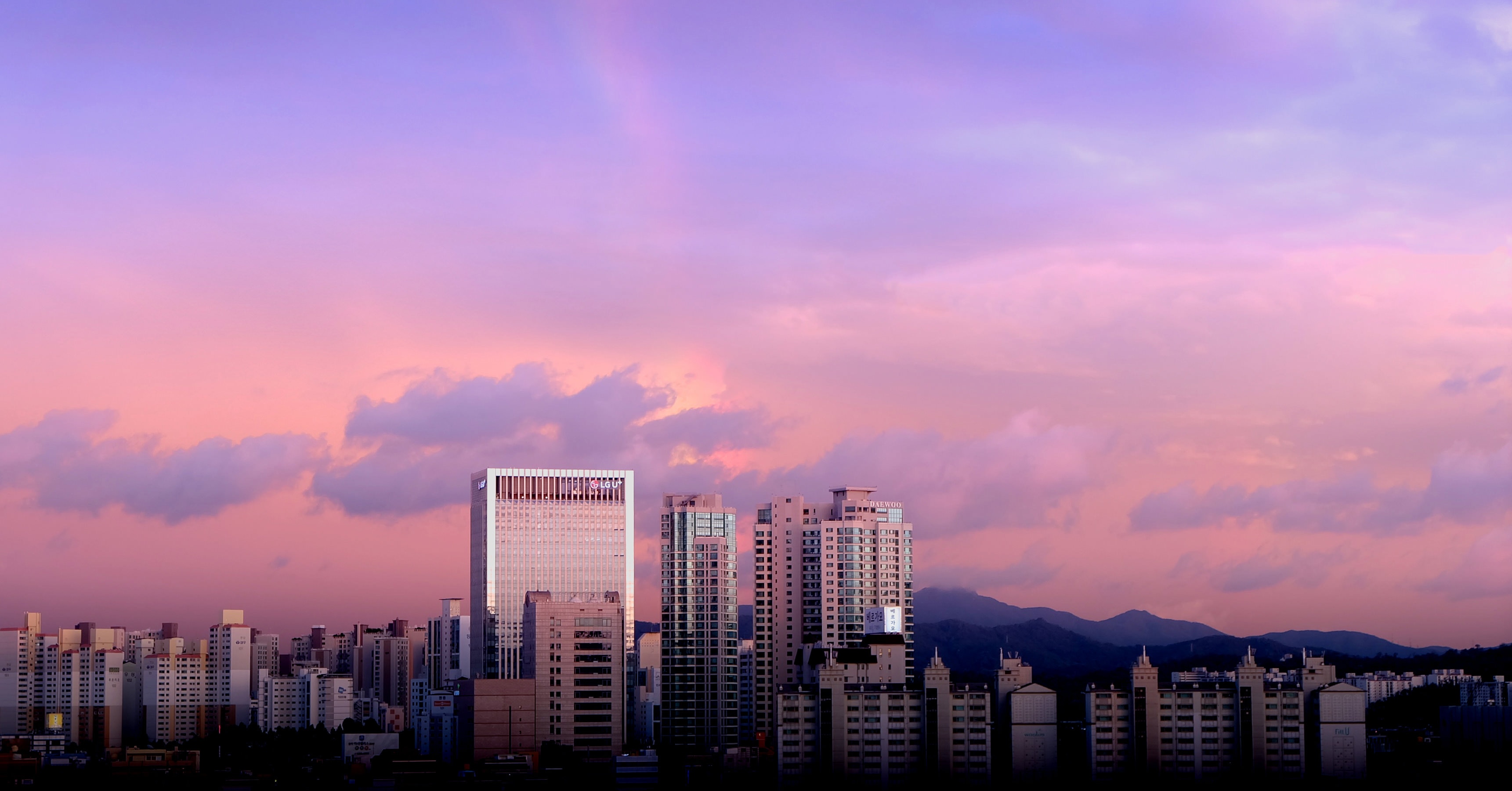 high rise buildings under purple and pink sky and clouds