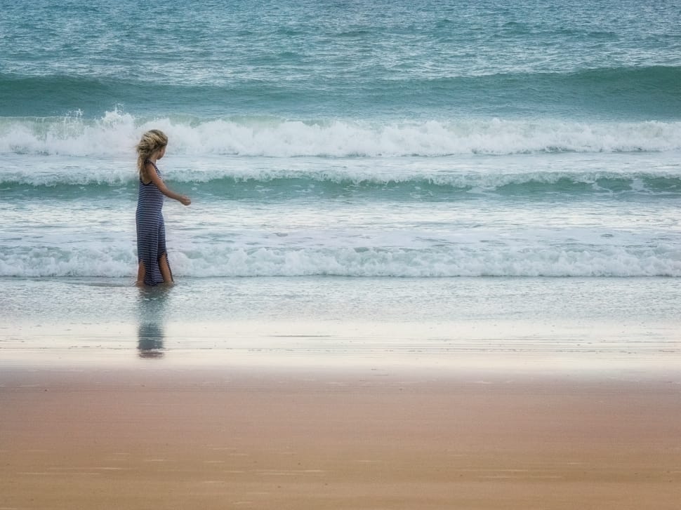 woman in blue dress standing on seashore during daytime preview