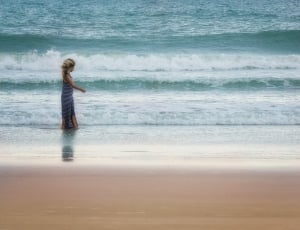 woman in blue dress standing on seashore during daytime thumbnail