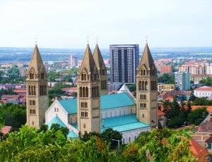 teal and beige church with four towers near green trees thumbnail