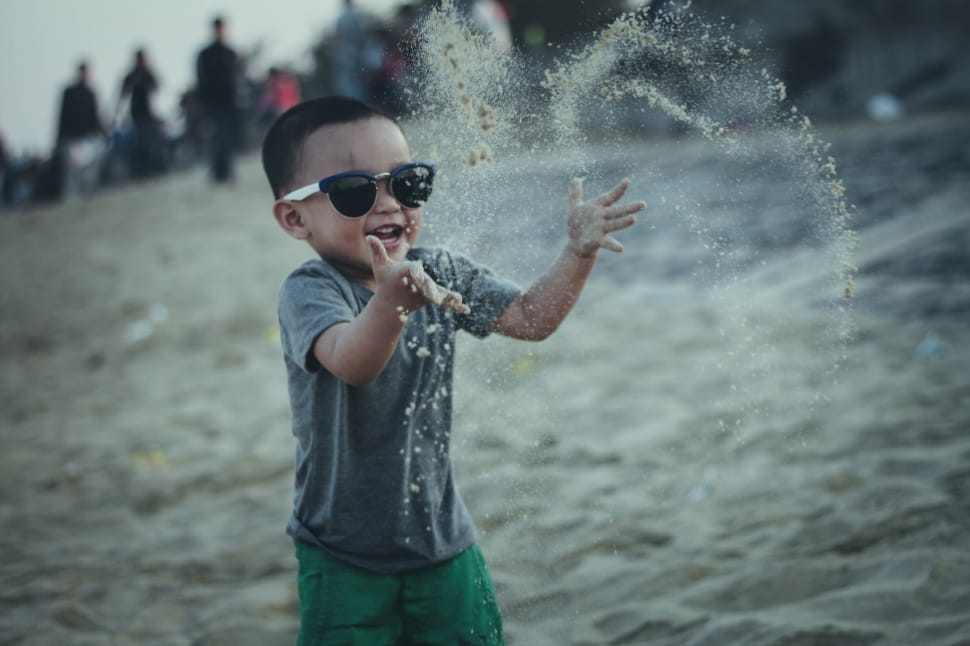 boy wearing black and white sunglasses playing sand at daytime preview