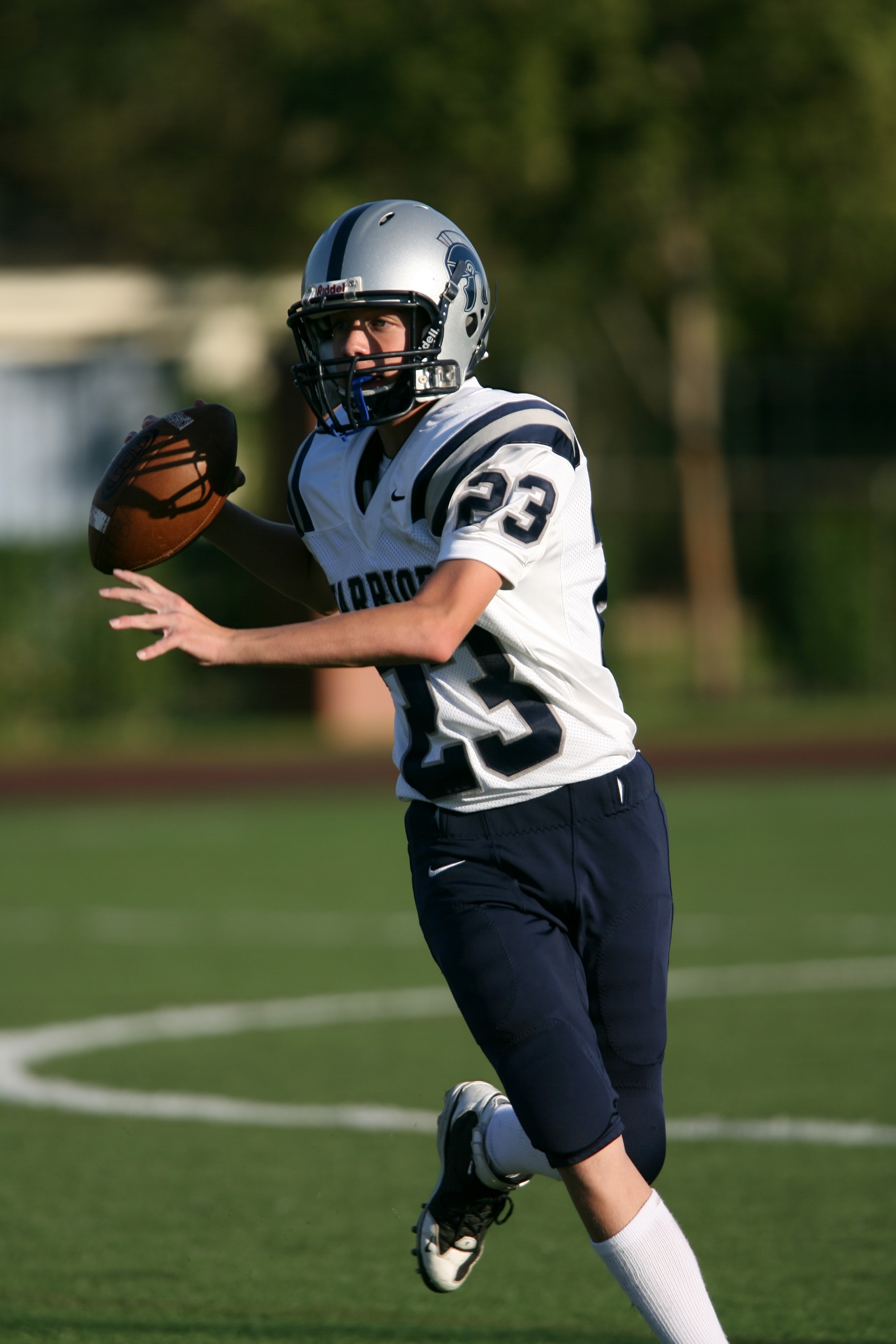 man in white and blue american football outfit holding a football while running at daytime