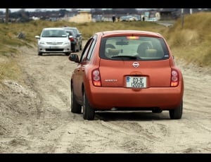 orange hatchback near two grey and black cars on road thumbnail