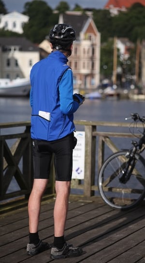 man in blue jacket and black shorts with bike helmet near body of water thumbnail