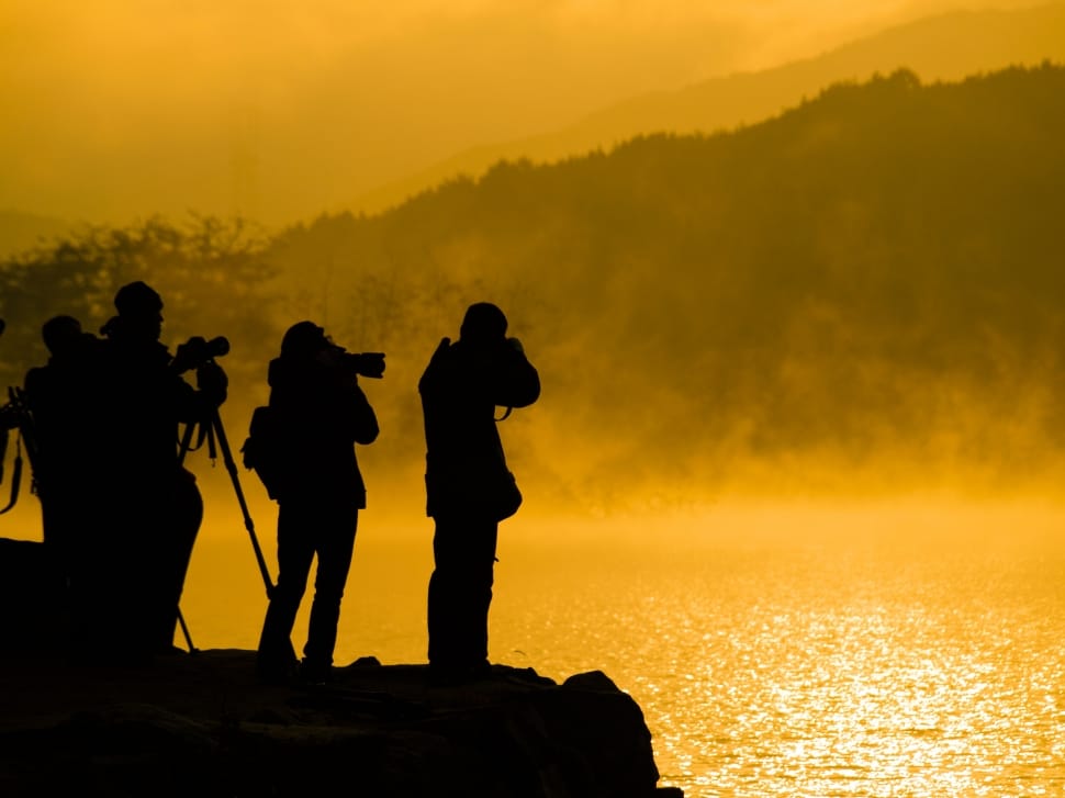silhoutte of people taking picture at the cliff near body of water preview