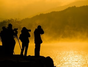 silhoutte of people taking picture at the cliff near body of water thumbnail