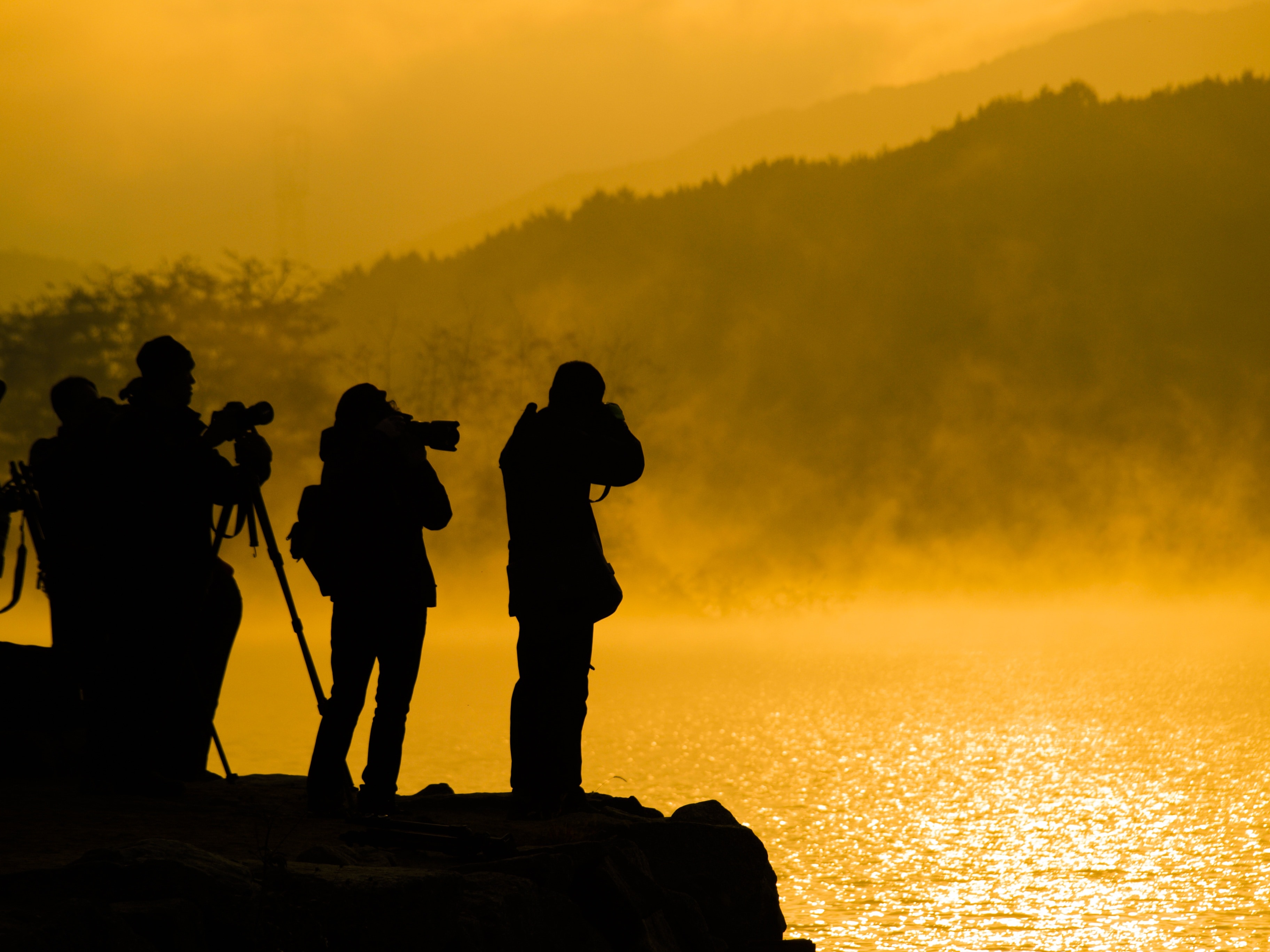 silhoutte of people taking picture at the cliff near body of water