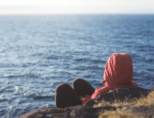 woman in red hoodie and black pants near body of water during daytime thumbnail