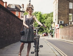 woman standing while holding a city bike at the street during daytime thumbnail