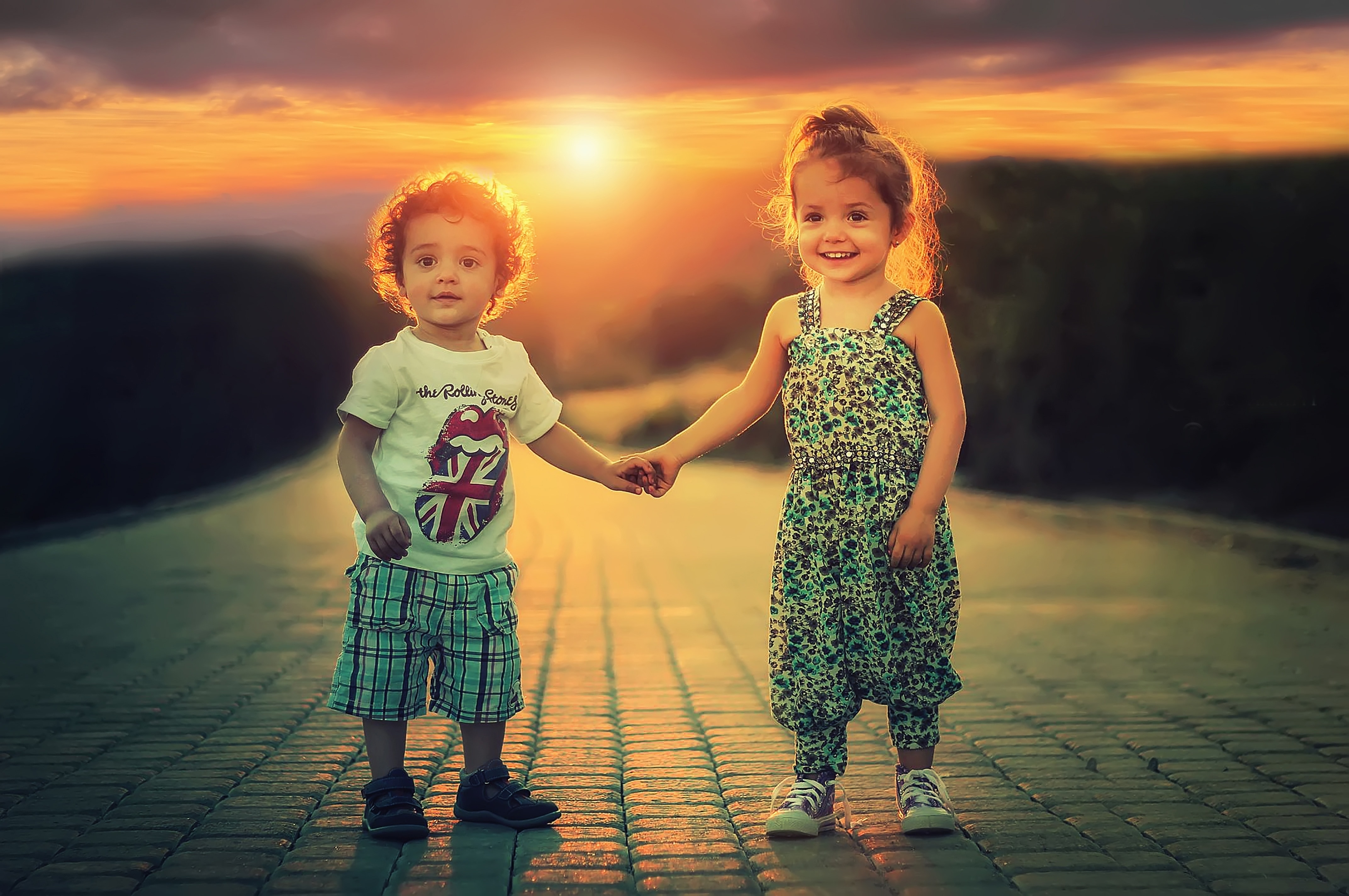 boy and girl holding hands on the road under sunset