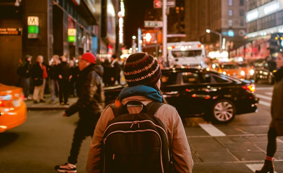person wearing knit hat and backpack walking along the street during nighttime preview
